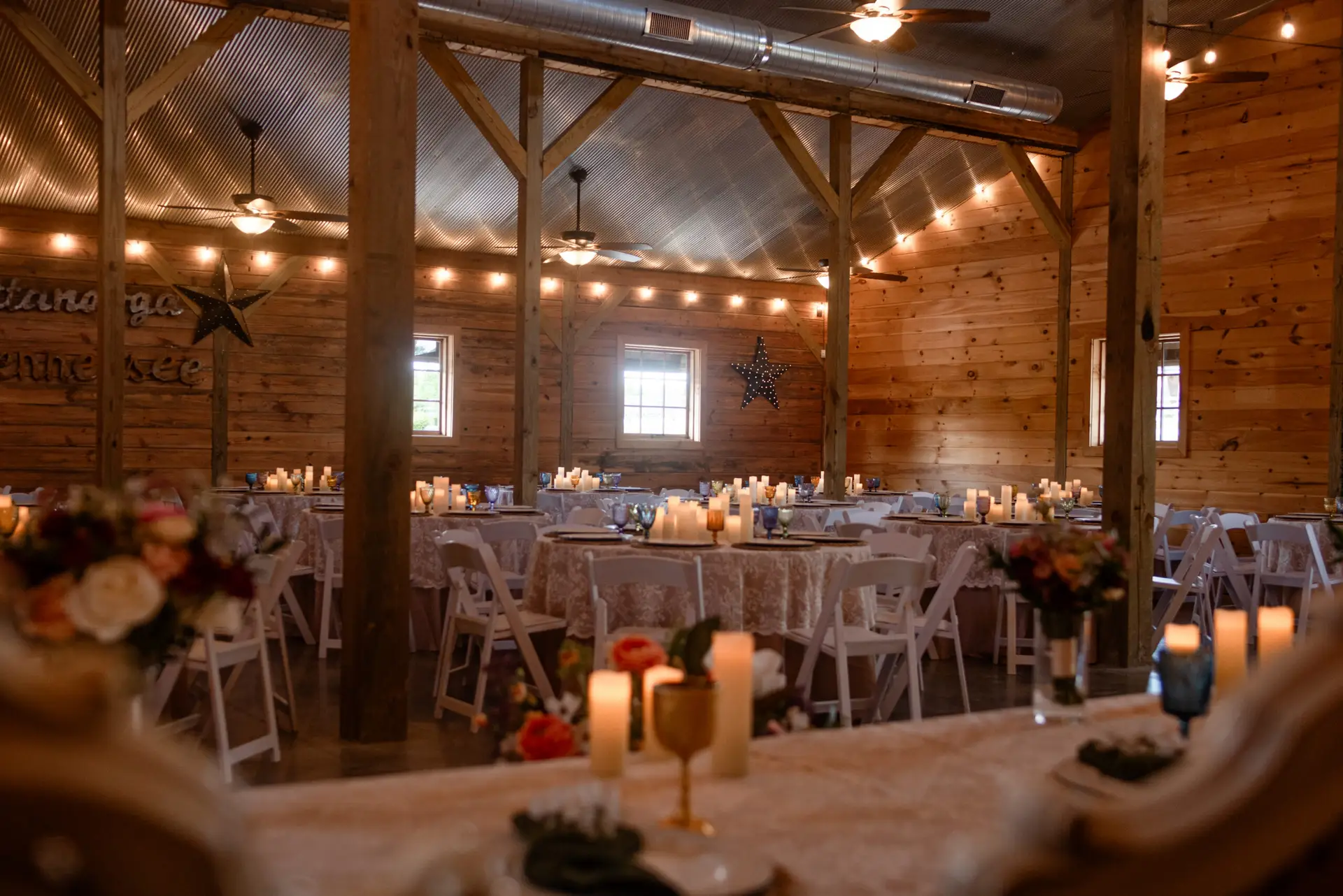 Candlelit barn reception with lace tables, string lights, and wood beams for Rachael & Ben at Covey Creek.