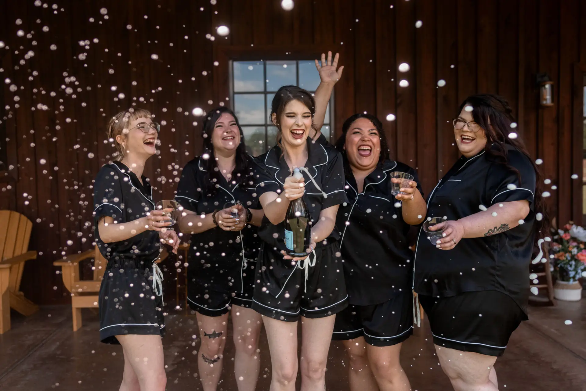 Rachael pops champagne with bridesmaids in black pajamas on the porch at Covey Creek, Rachael & Ben.