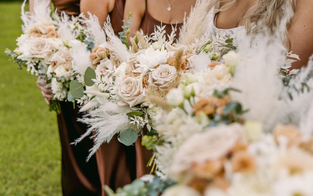 Alexis & Logan bridesmaids in copper satin hold cream rose and pampas bouquets outdoors at Covey Creek