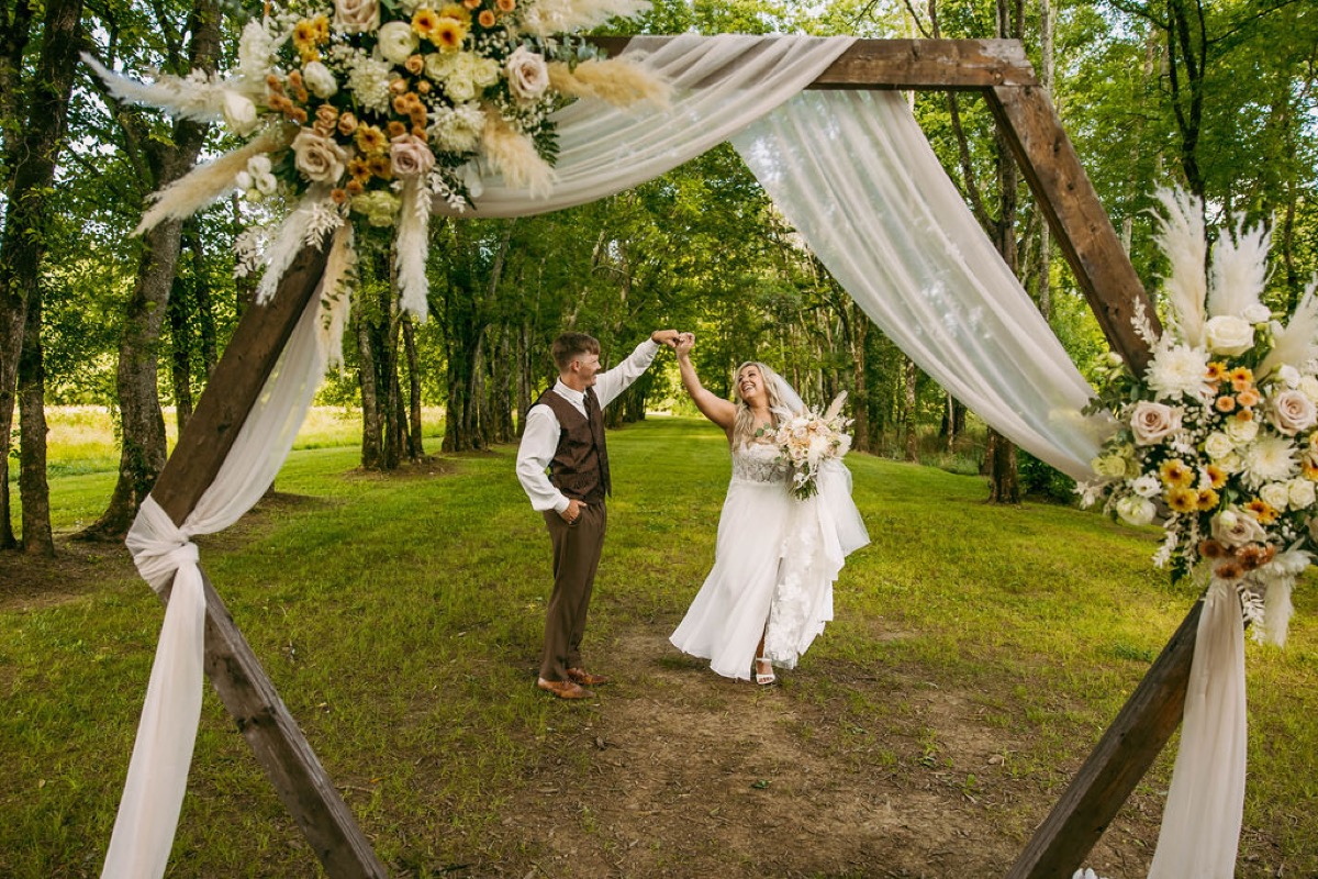 Alexis & Logan spin under the floral hexagonal arch along the tree-lined path at Covey Creek