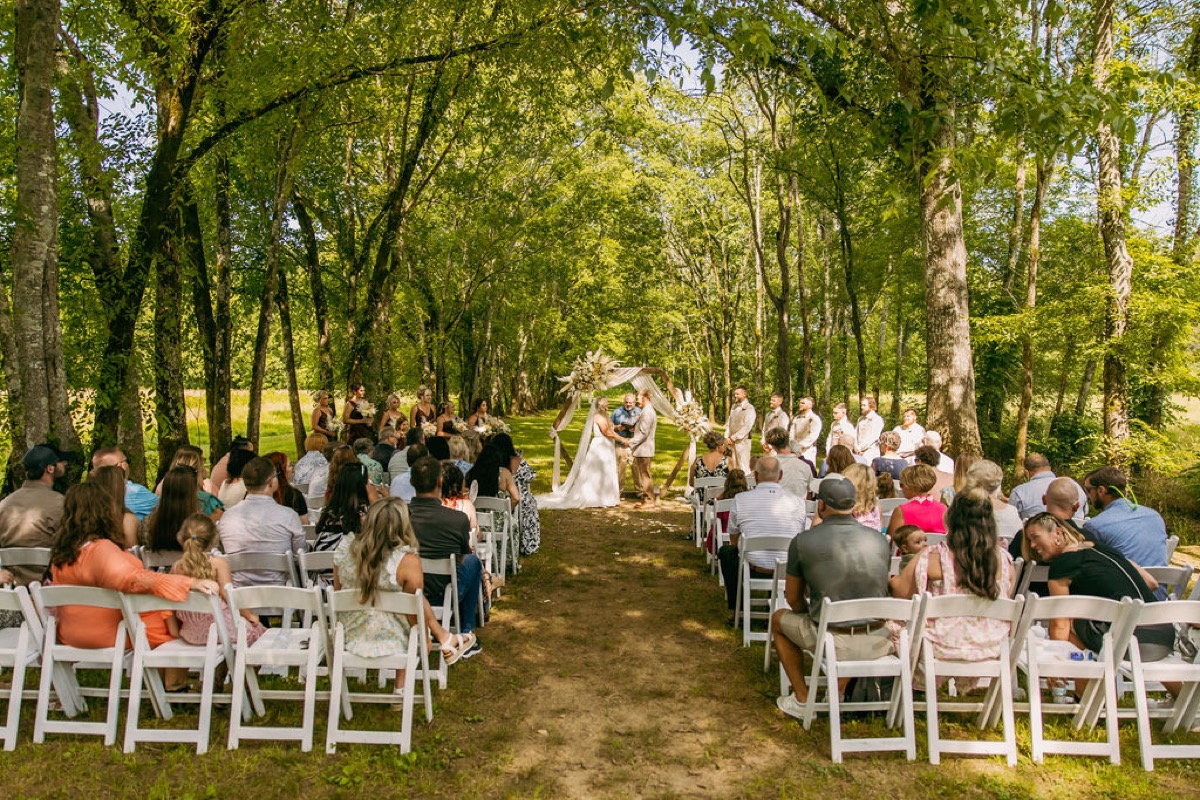 Alexis & Logan exchange vows under a hex arch as guests watch in the Tunnel of Love at Covey Creek