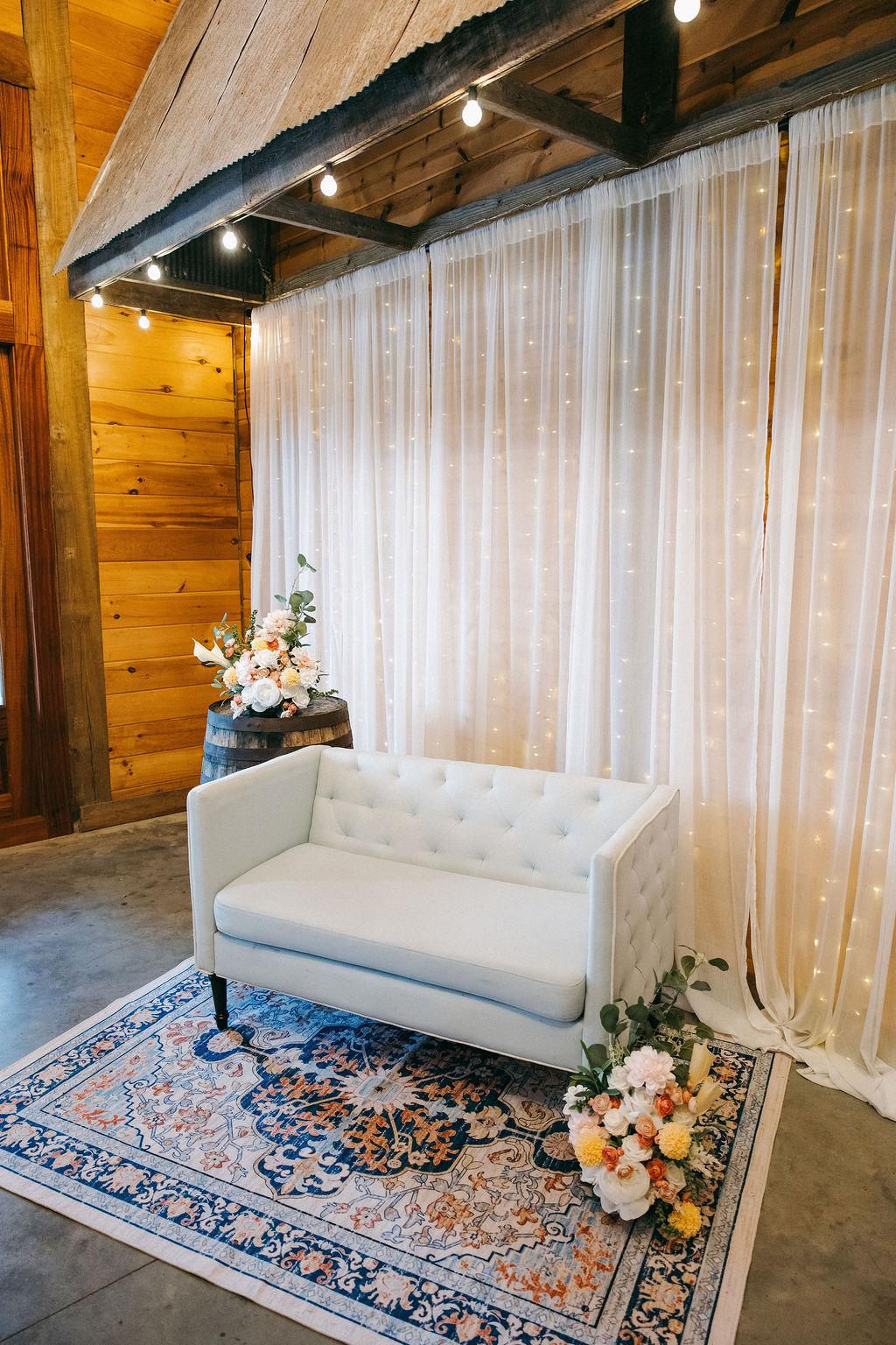 Amanda & Stephen’s reception lounge at Covey Creek with tufted sofa, barrel florals, and fairy lights