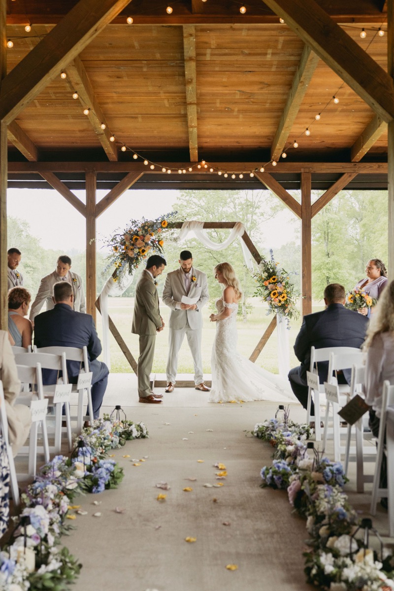 Brianna & Michael exchange vows before a sunflower hexagonal arbor as guests fill Covey Creek's open patio pavilion.