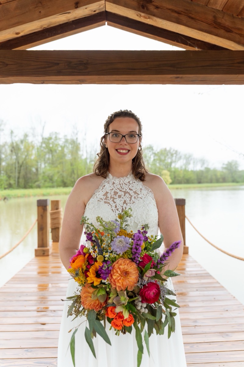 Caitlin & Daniel: bride Caitlin holds a bright wildflower bouquet on the Pond dock at Covey Creek