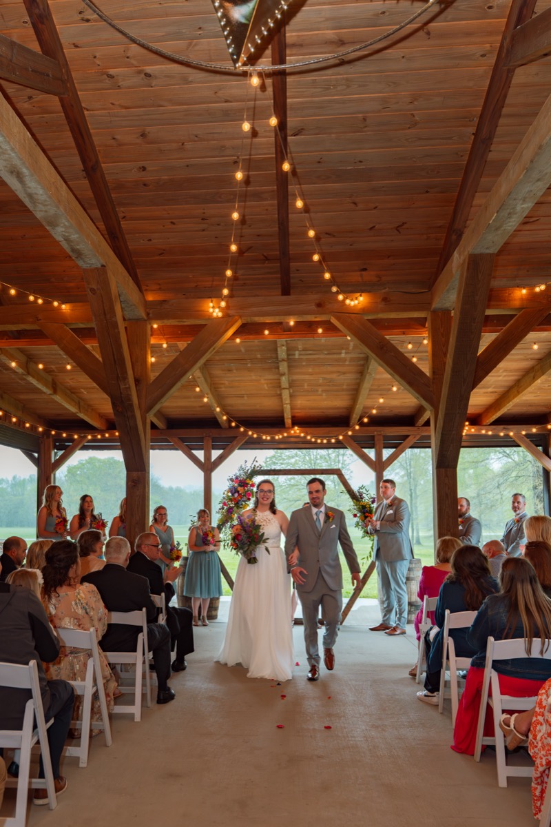 Caitlin & Daniel recess down the Pond pavilion aisle past guests and a floral hex arch at Covey Creek