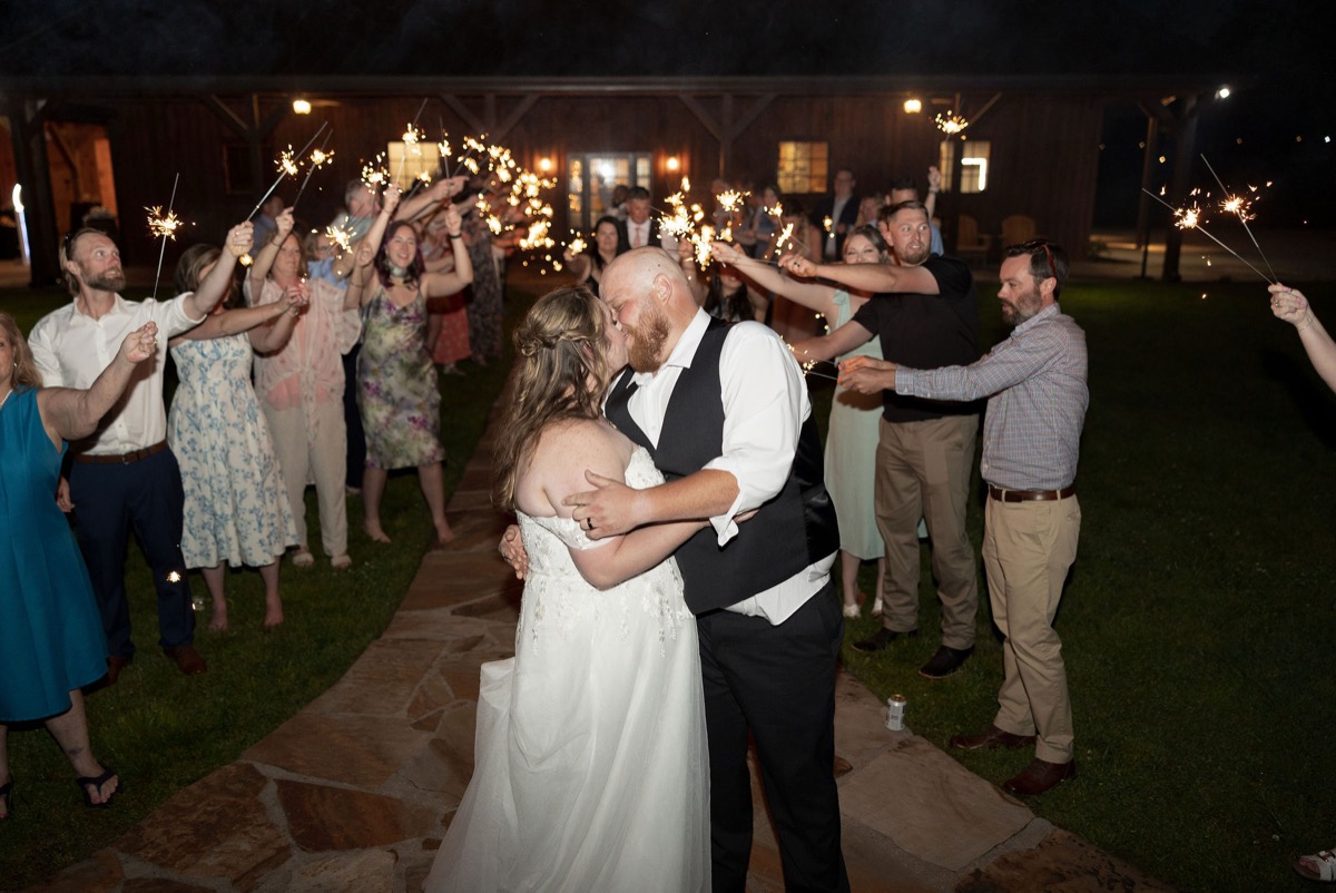 Carly & Lucas kiss amid guest sparklers on the Patio stone path at Covey Creek for their send-off