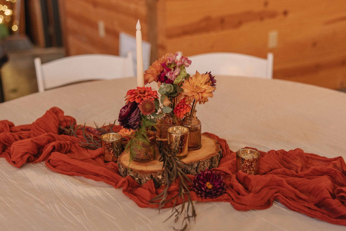 Claire & Jacob table with amber bud vases, autumn blooms, and orange runner in the barn at Covey Creek