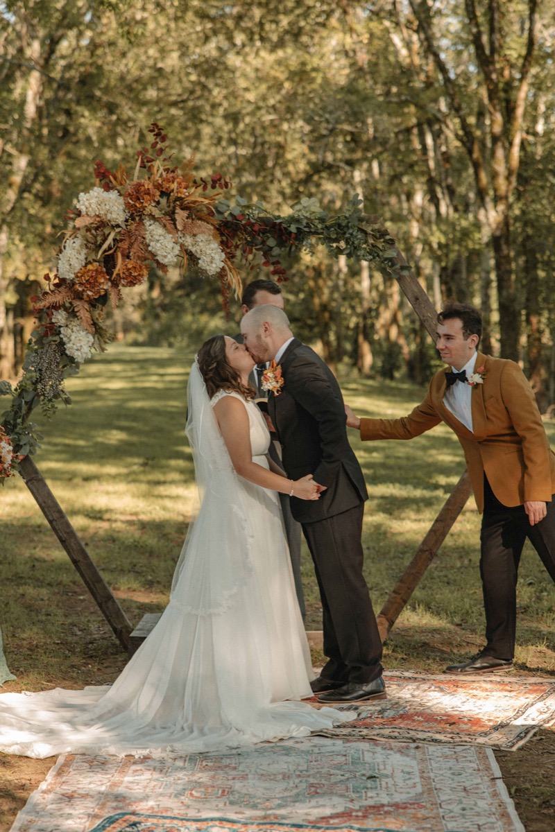 Claire & Jacob share their first kiss under a floral wooden hexagon arch outdoors at Covey Creek