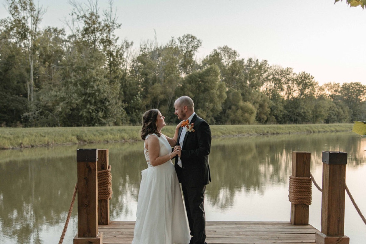 Claire & Jacob hold hands on the Pond dock with tree reflections in still water at Covey Creek