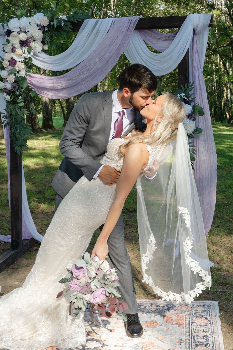 Courtney & Brett share a dip kiss under their fabric-draped floral arbor at Covey Creek ceremony