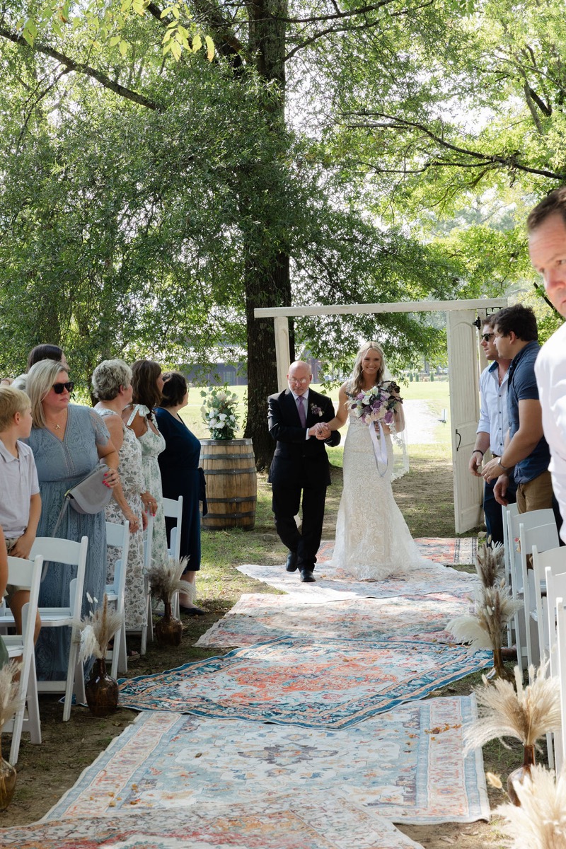 Courtney & Brett: bride walks the patterned rug aisle with her father at their Covey Creek outdoor ceremony
