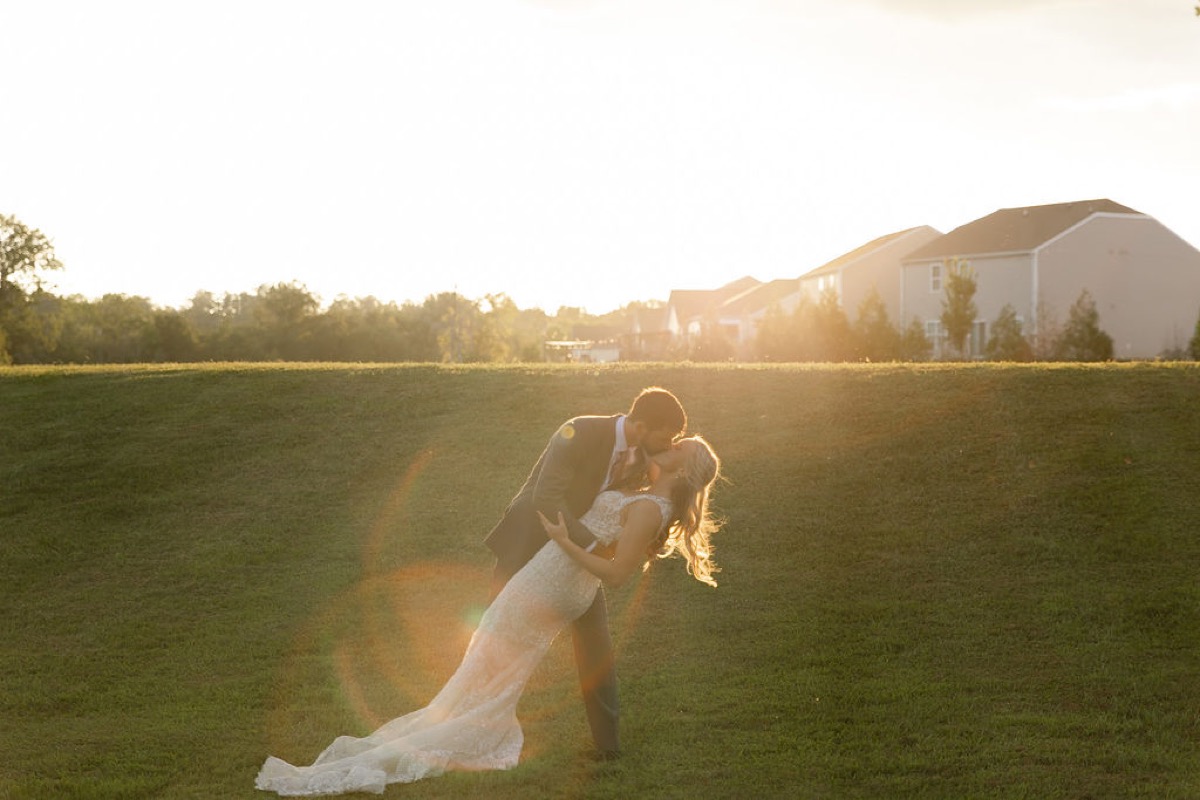 Courtney & Brett share a sunset dip kiss in an open field with warm lens flare at Covey Creek