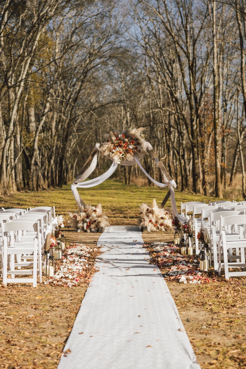 White petal-strewn aisle and lanterns lead to Danika & Troy's pampas wood arch at Covey Creek