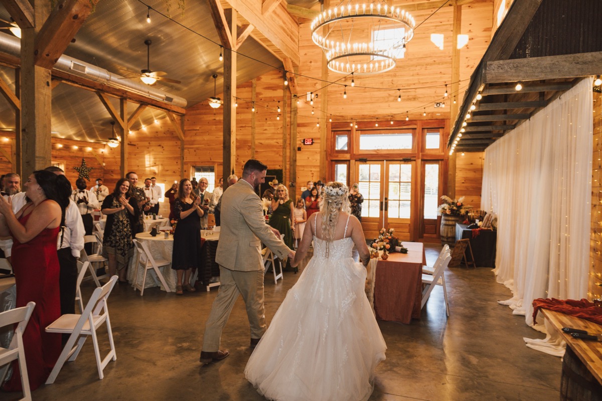 Danika & Troy enter the barn reception as guests cheer under chandelier lights at Covey Creek