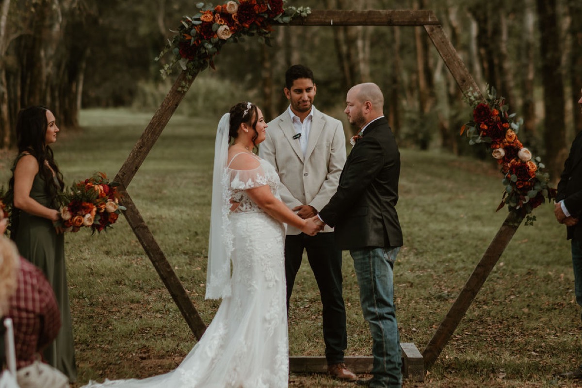Elizabeth & Ashton hold hands under a flowered hexagonal arbor during their outdoor ceremony at Covey Creek