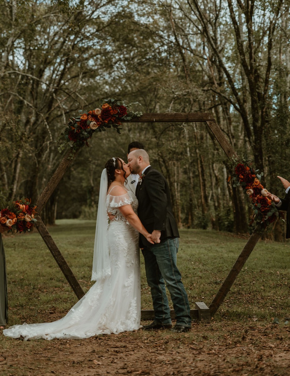 Elizabeth & Ashton share their first kiss under a flowered hexagonal arbor in the trees at Covey Creek