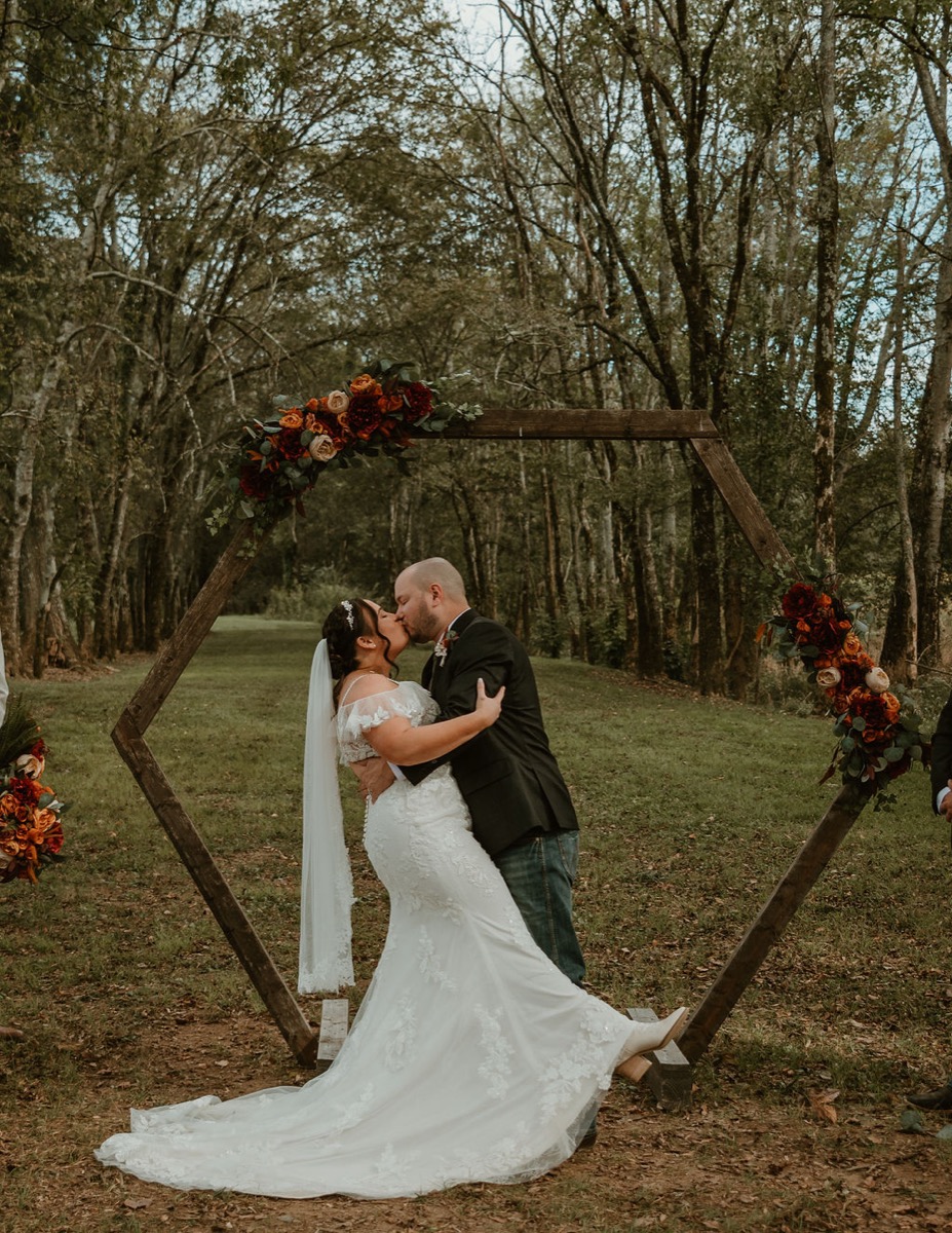 Elizabeth & Ashton share a dip kiss framed by Covey Creek’s hexagonal arbor and autumn floral clusters