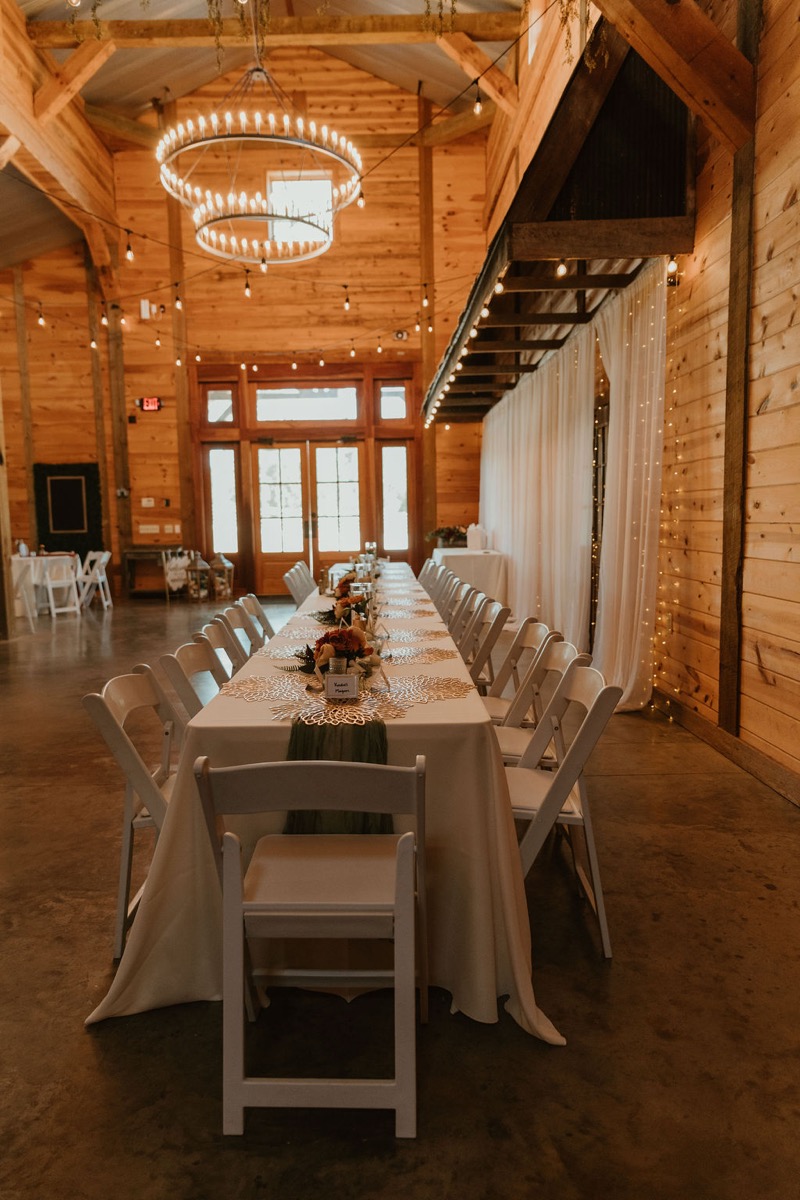 Long banquet table for Elizabeth & Ashton at Covey Creek with green runner, gold placemats, and barn chandeliers