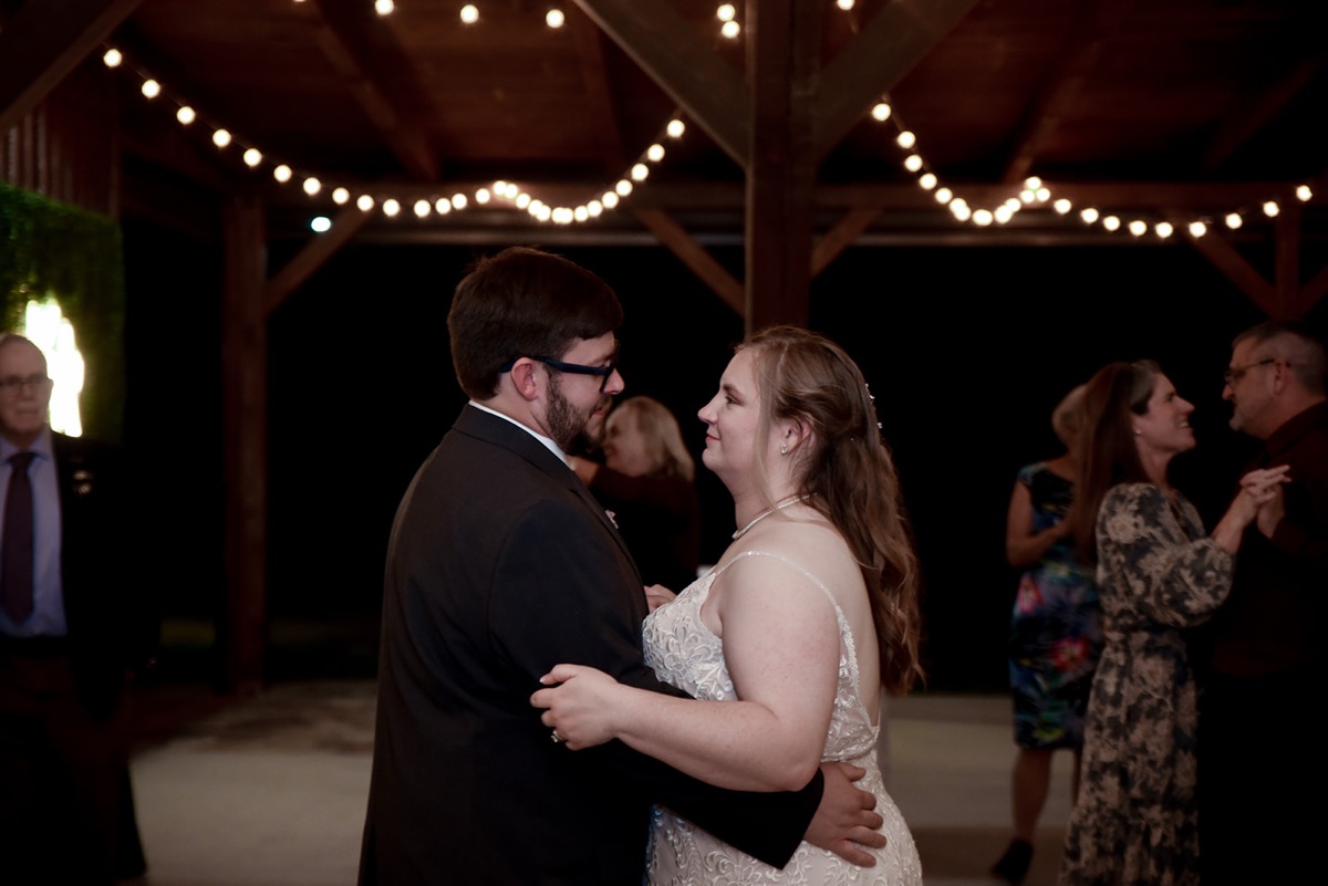 Emily & Jared share a first dance under warm string lights in a wooden pavilion at night at Covey Creek.