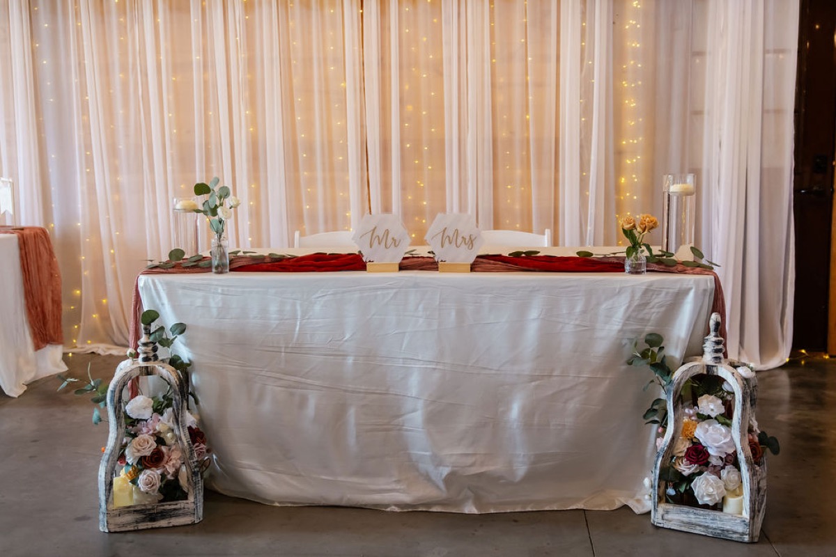 Erica & Randall sweetheart table with Mr & Mrs signs, burgundy runner, and fairy-lit curtains at Covey Creek