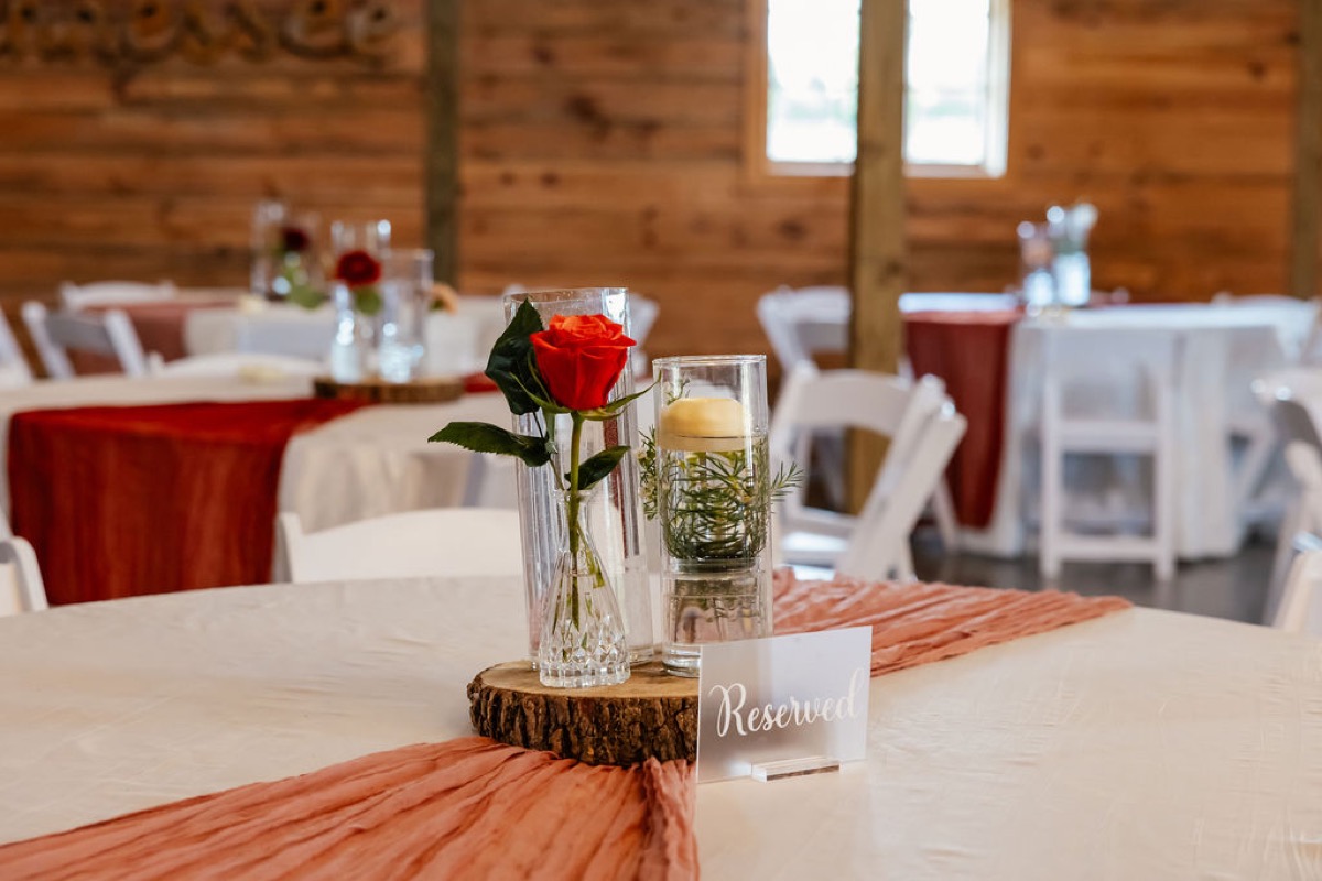 Erica & Randall reserved table with red rose, floating candle on wood slice, and terracotta runner at Covey Creek