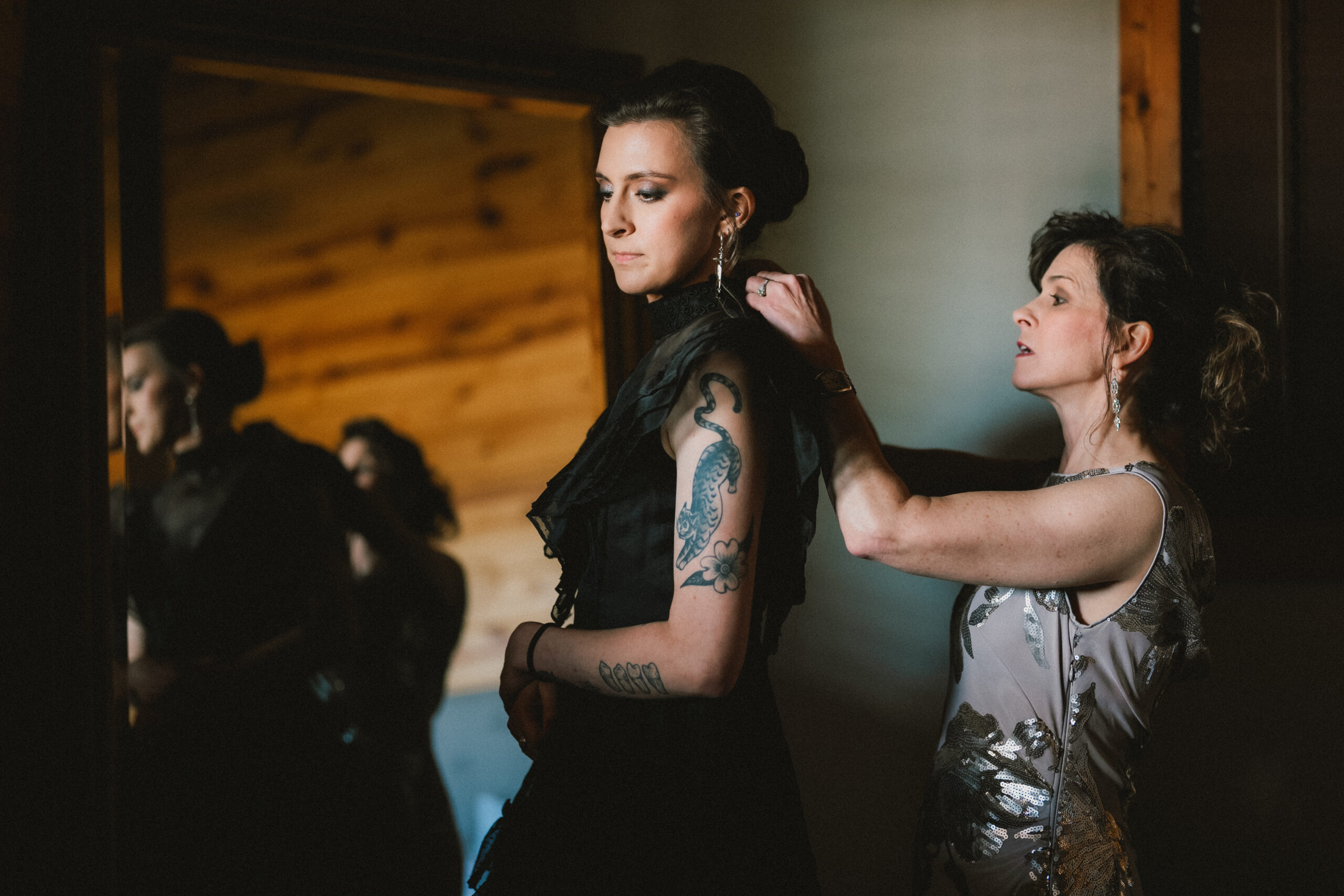 Erin & Baxter's wedding: Erin has her black ruffled gown adjusted by a wood mirror at Covey Creek