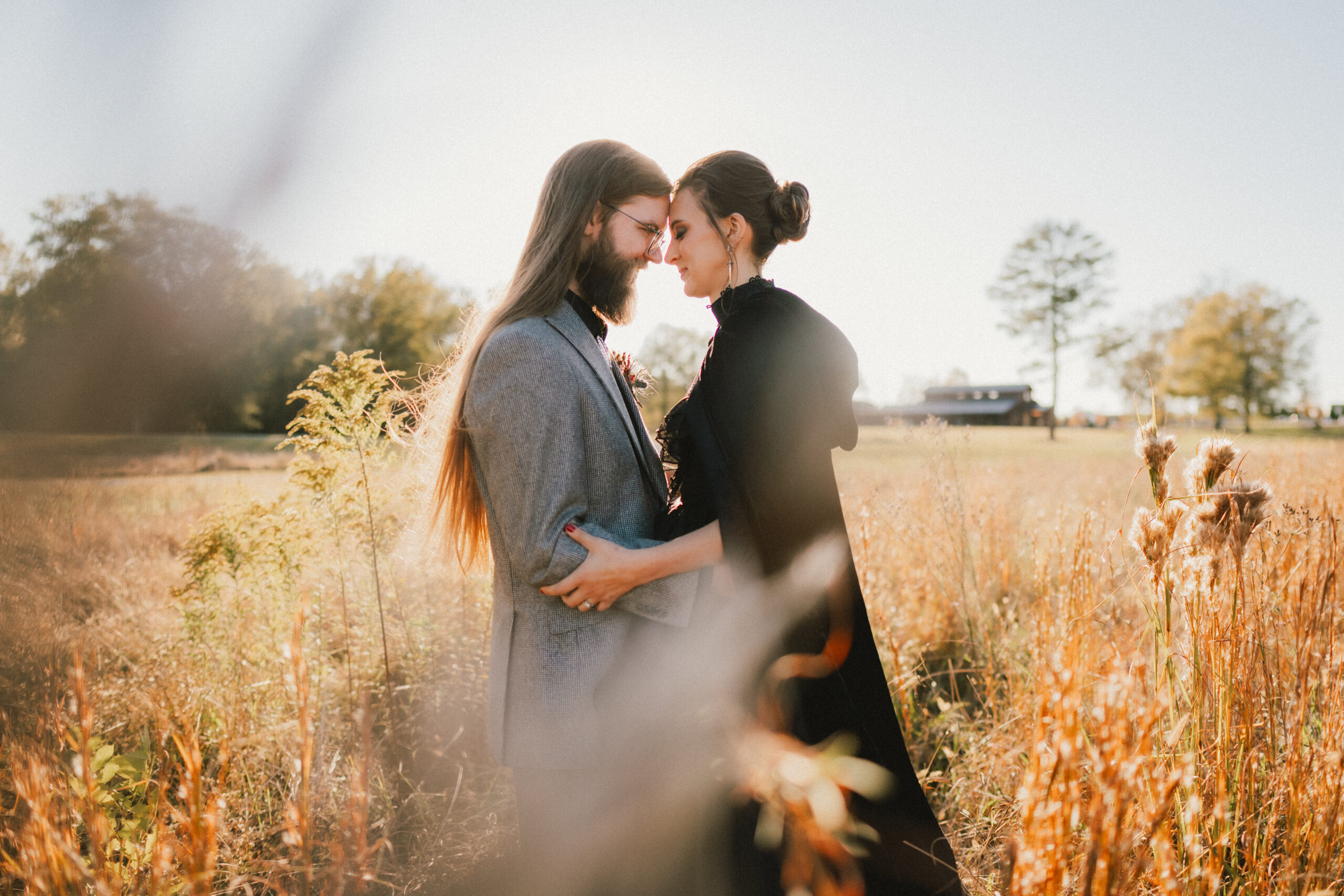 Erin & Baxter press foreheads in tall golden grass with the barn behind them at Covey Creek