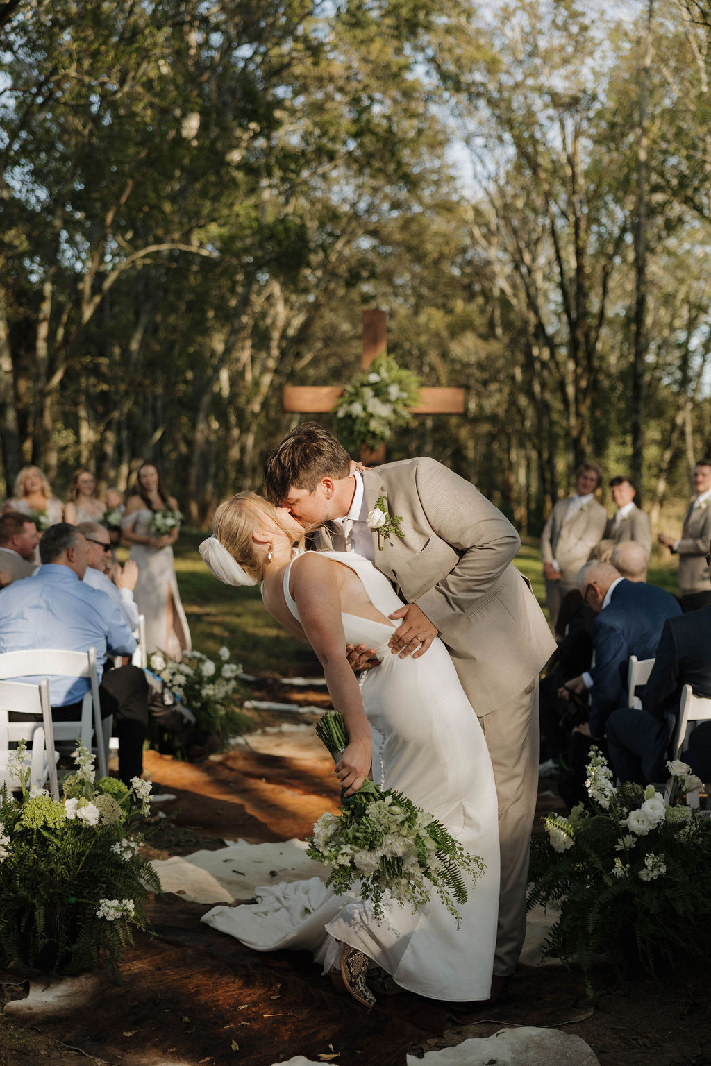 Joseph dips Hailey for a kiss on the cowhide aisle before a wooden cross at Hailey & Joseph's Covey Creek wedding