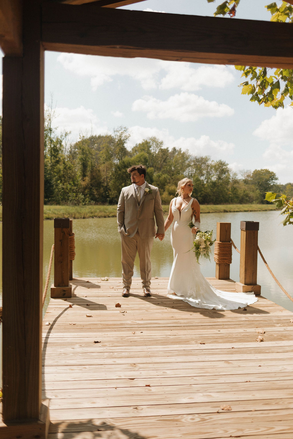 Hailey & Joseph stand hand-in-hand on the wooden Pond dock overlooking the water at Covey Creek