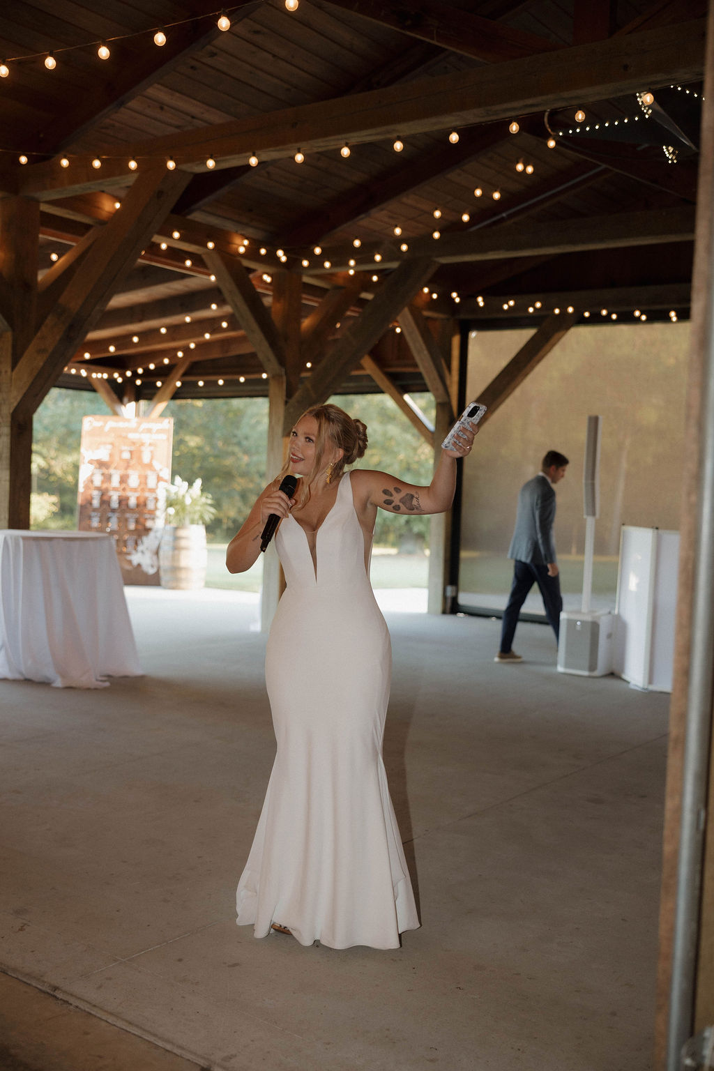 Hailey toasts with a mic under string lights in the pavilion at Hailey & Joseph's Covey Creek wedding