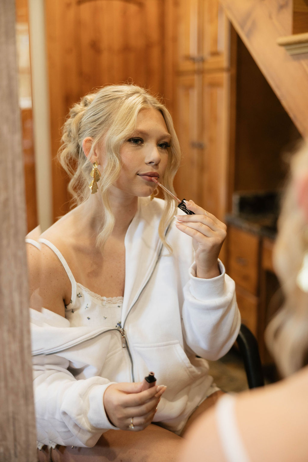 Hailey applies lip gloss in a mirror while getting ready for Hailey & Joseph's wedding at Covey Creek