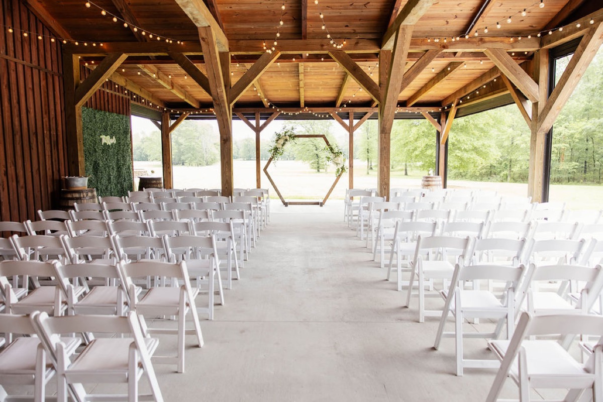 White chairs face a flowered hexagonal arch in Covey Creek's patio pavilion for Hannah & Nicholas's ceremony.