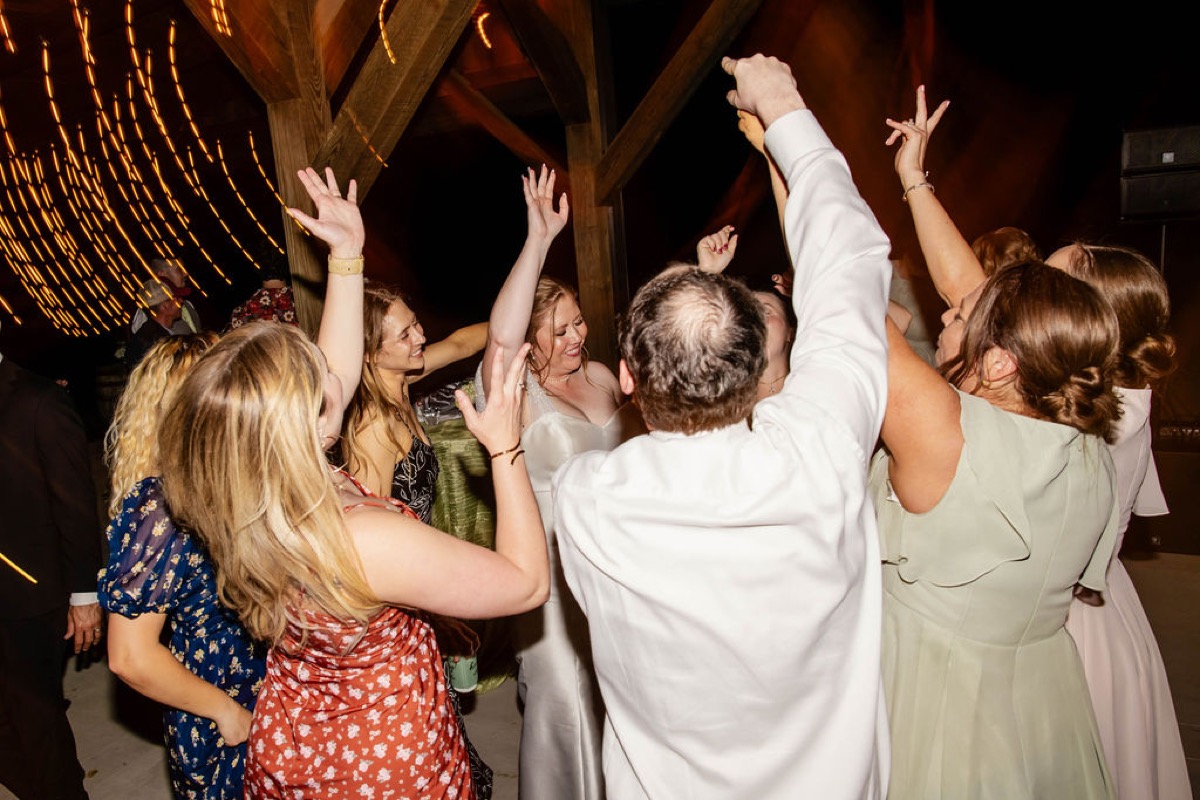 Hannah & Nicholas dance with arms raised as string lights blur at Covey Creek's night reception.