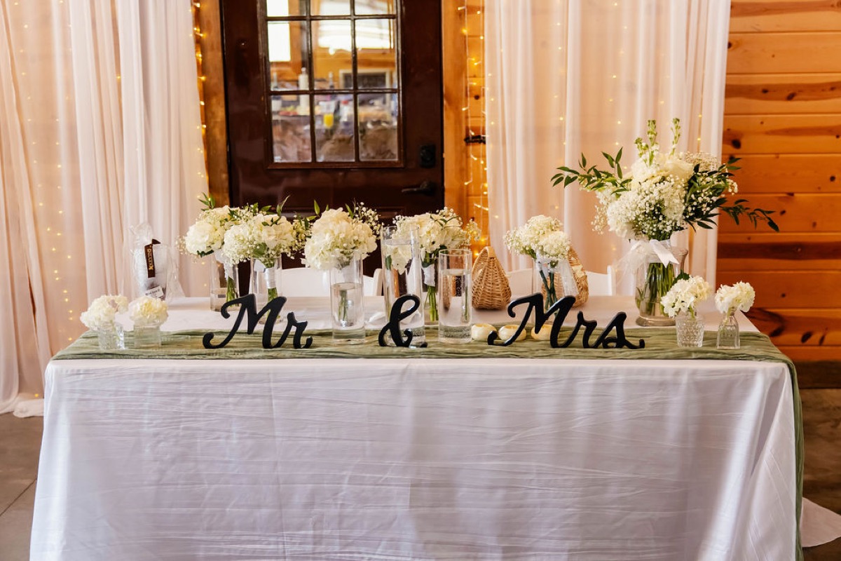 Hannah & Nicholas sweetheart table with Mr & Mrs sign, white florals, and glowing curtains at Covey Creek.