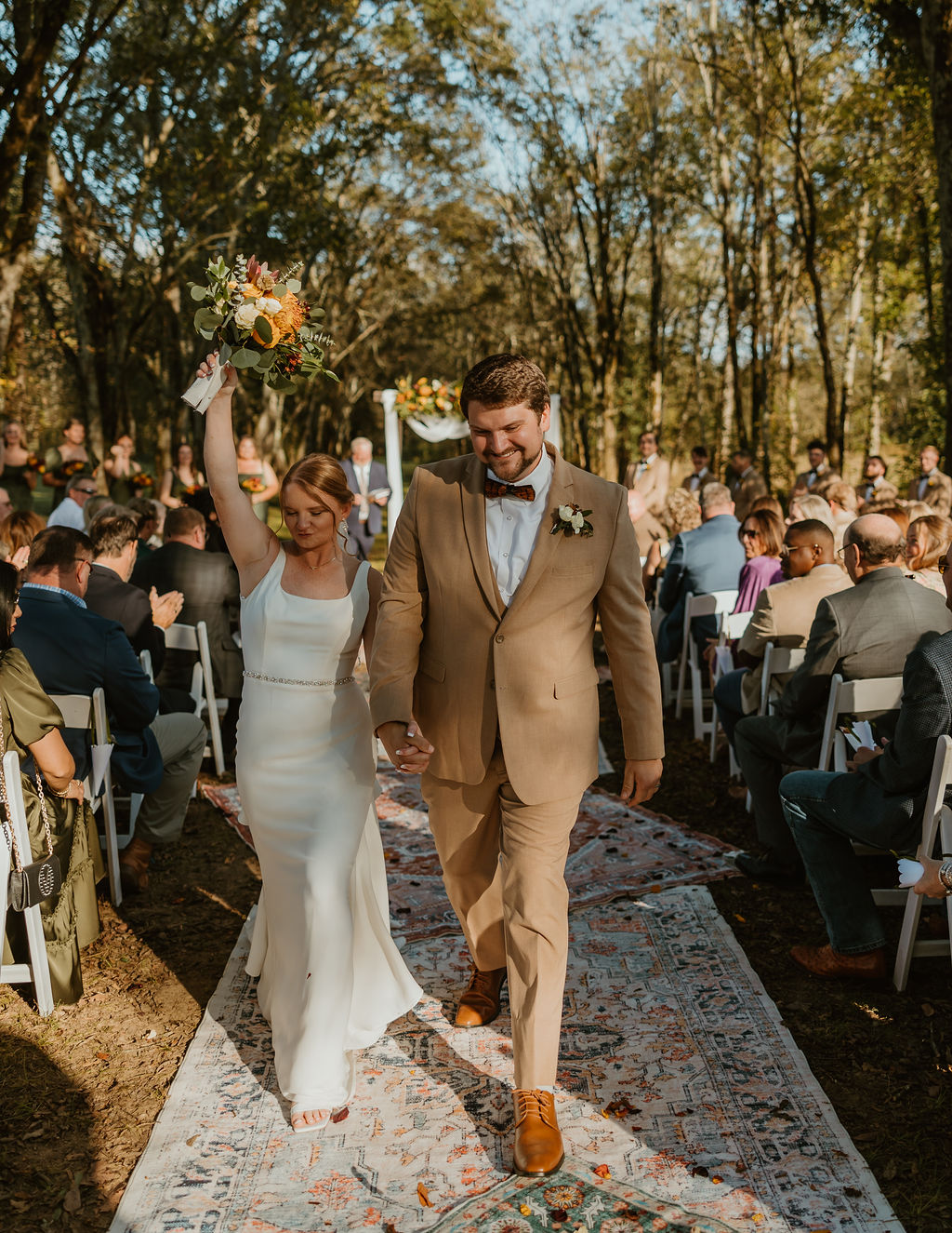 JJ & Will recess down the Tunnel of Love rug aisle, bouquet raised, guests cheering at Covey Creek