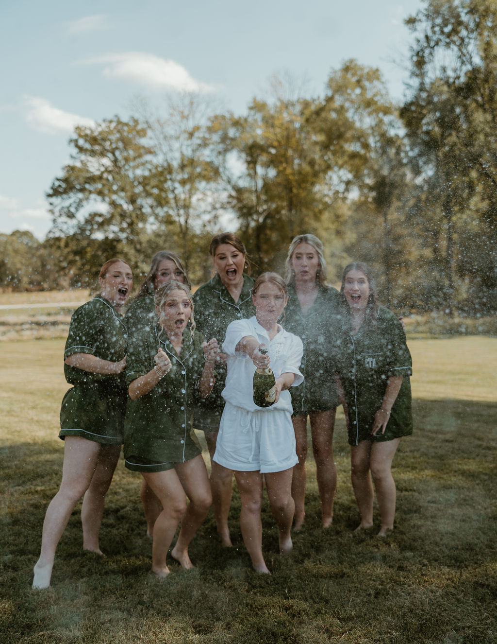 JJ & Will: bride JJ sprays champagne with bridesmaids in forest-green pajamas on the lawn at Covey Creek