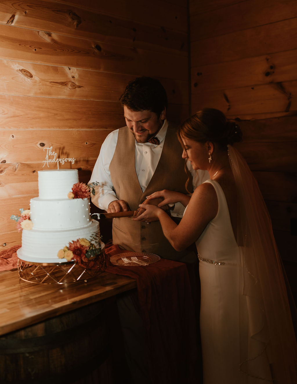 JJ & Will cut their three-tier white Andersons cake with fall florals indoors at Covey Creek