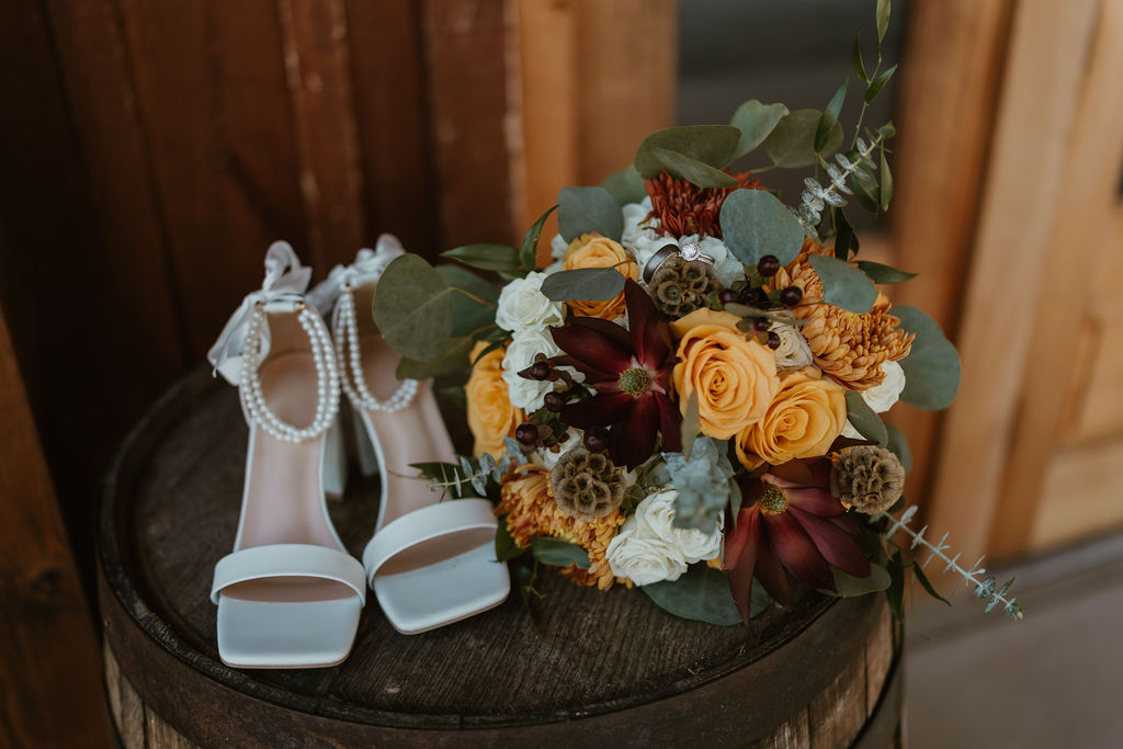 JJ & Will bridal shoes with pearl straps, autumn bouquet, and rings on a barrel at Covey Creek