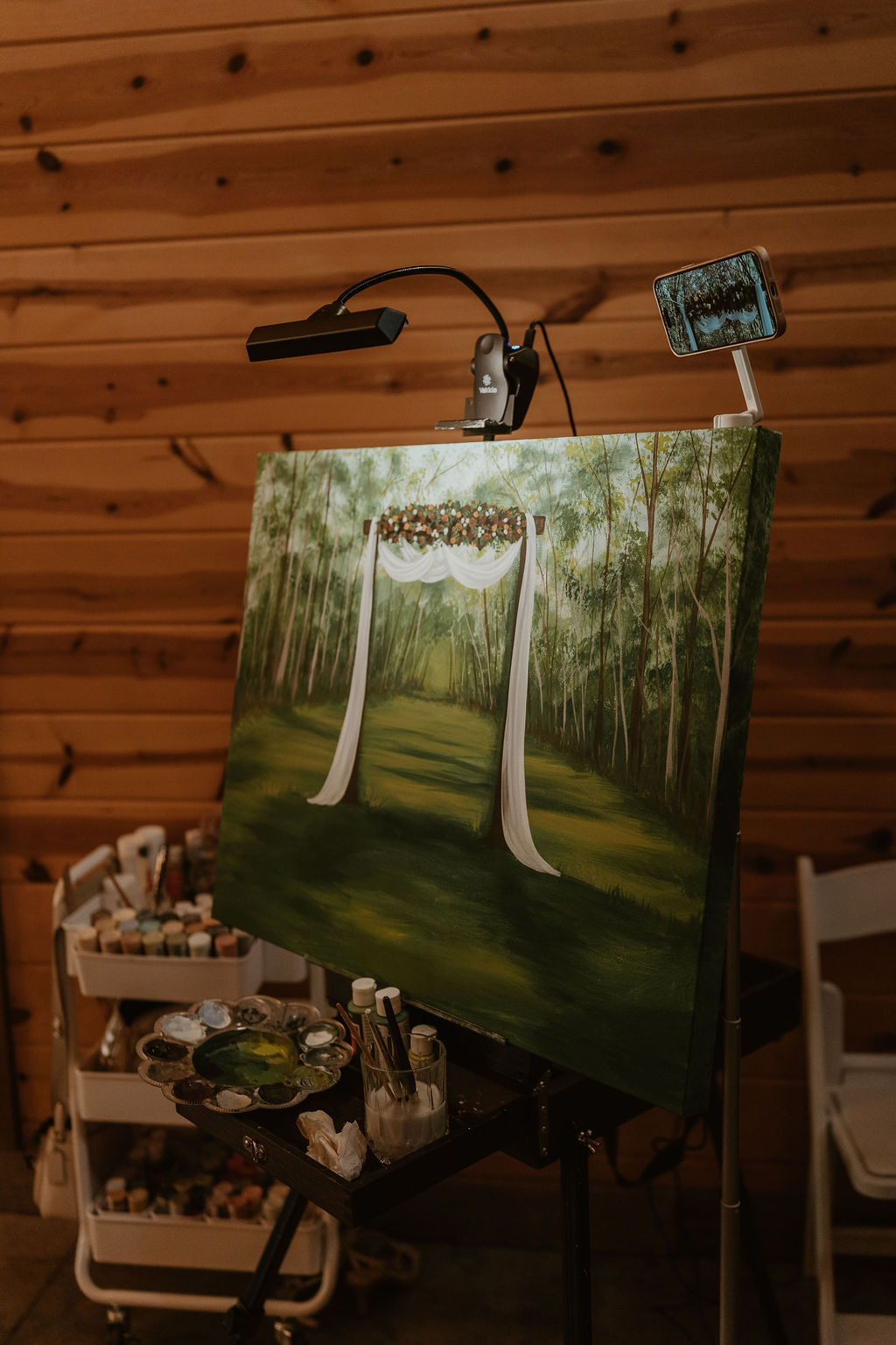 JJ & Will live painter's easel shows their Tunnel of Love arbor scene mid-reception at Covey Creek