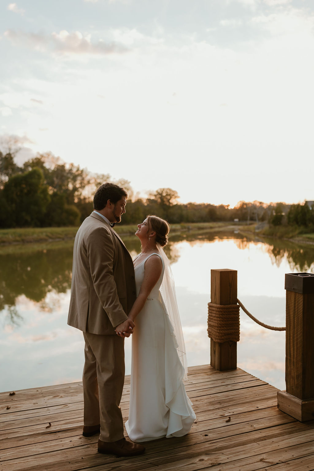JJ & Will stand close on the Pond dock at sunset, holding hands over calm water at Covey Creek