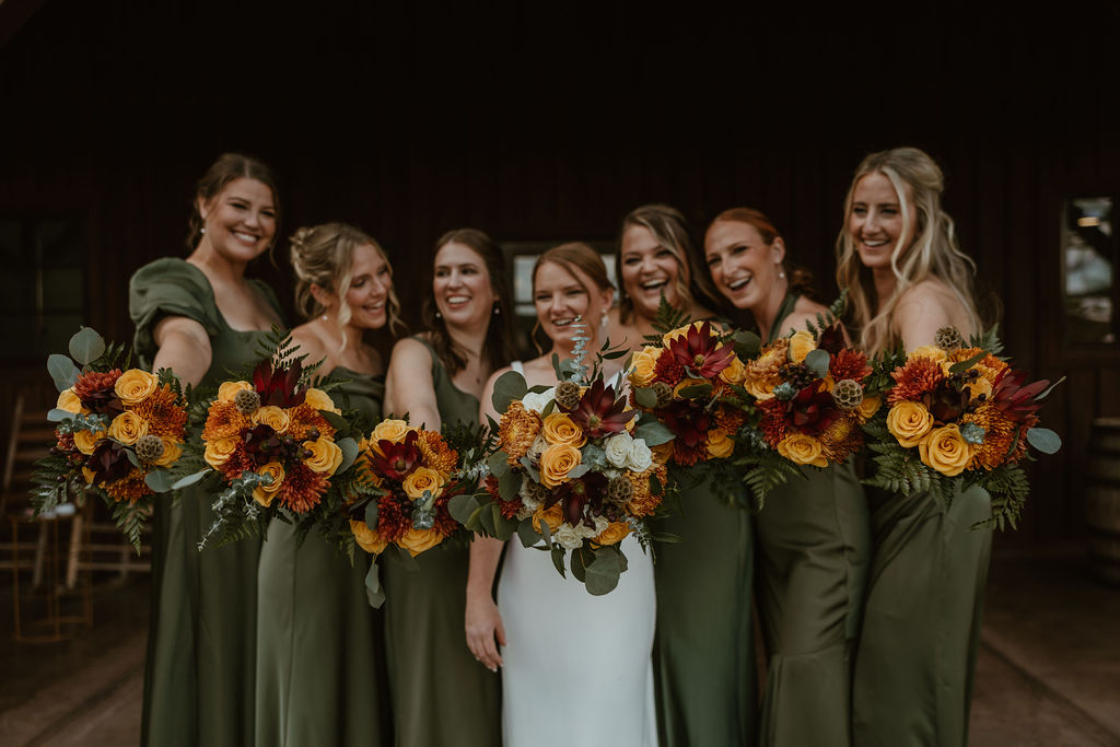 JJ & Will: bride JJ and olive-green bridesmaids hold autumn bouquets by the barn at Covey Creek