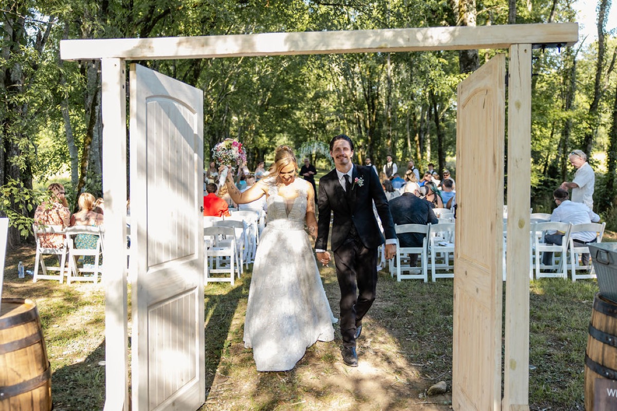 Kolbe & Nathan smile walking through wooden aisle doors after their ceremony at Covey Creek