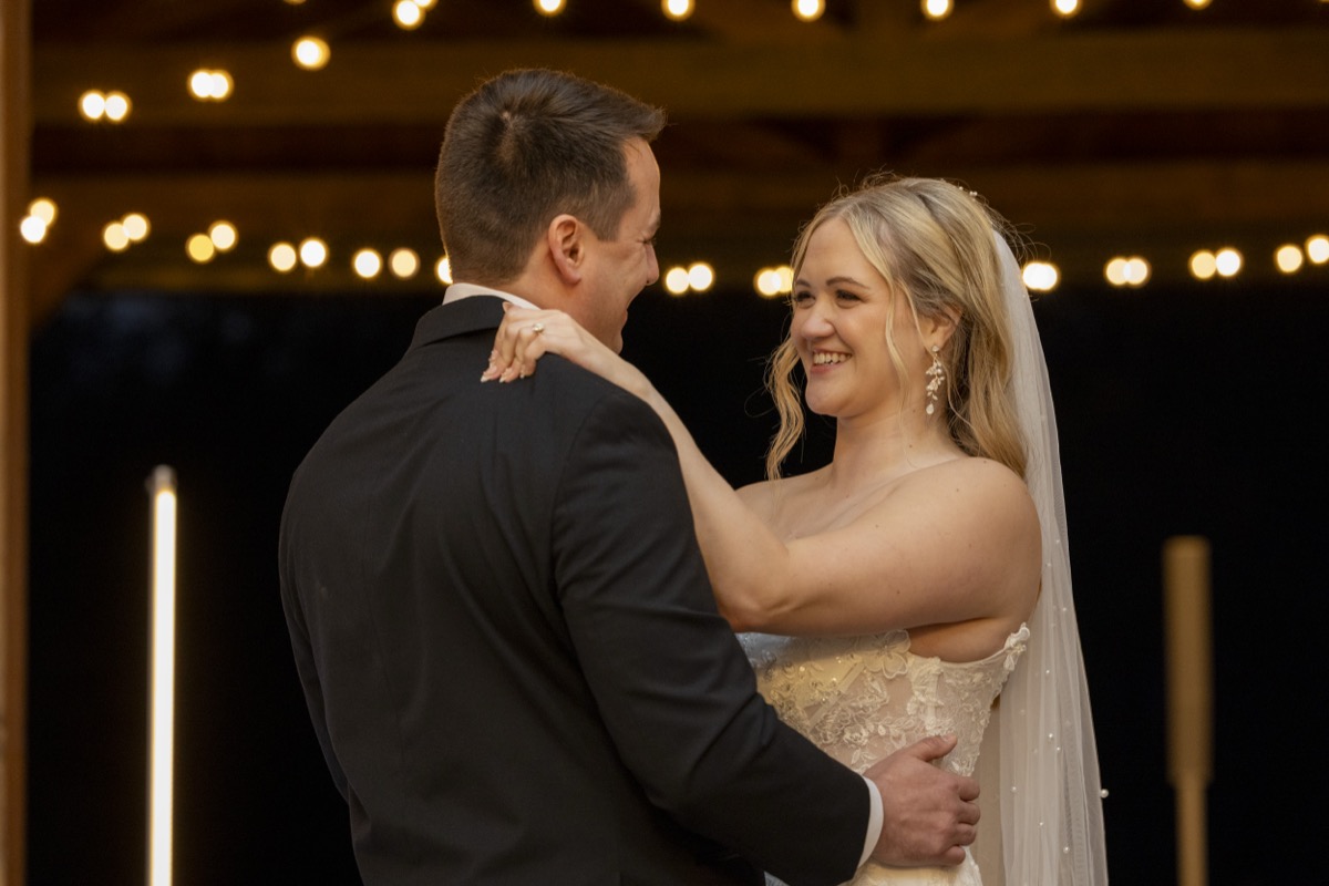 Kristen & Dalton dance under warm string lights, her pearl-veiled lace gown glowing at Covey Creek