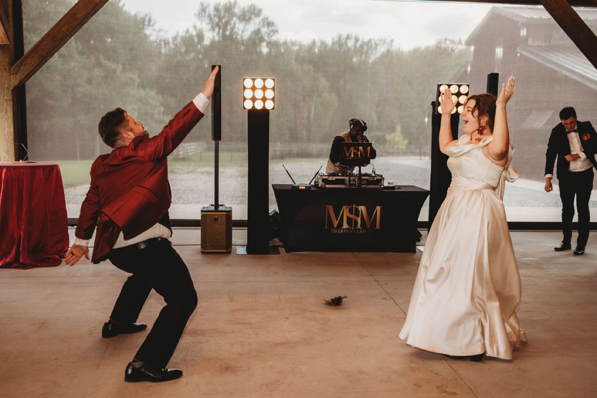 Lauren & Alex dance energetically with arms raised facing each other in the barn at Covey Creek