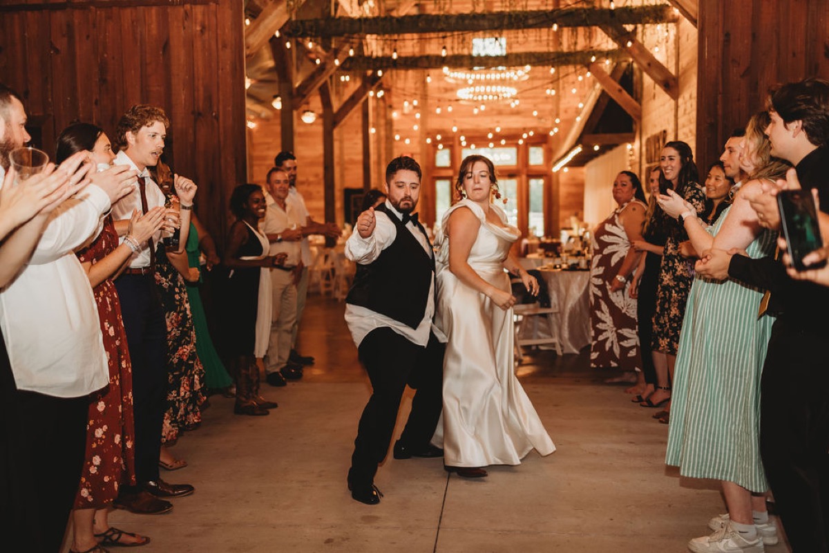 Lauren & Alex dance through a tunnel of cheering guests under barn string lights at Covey Creek