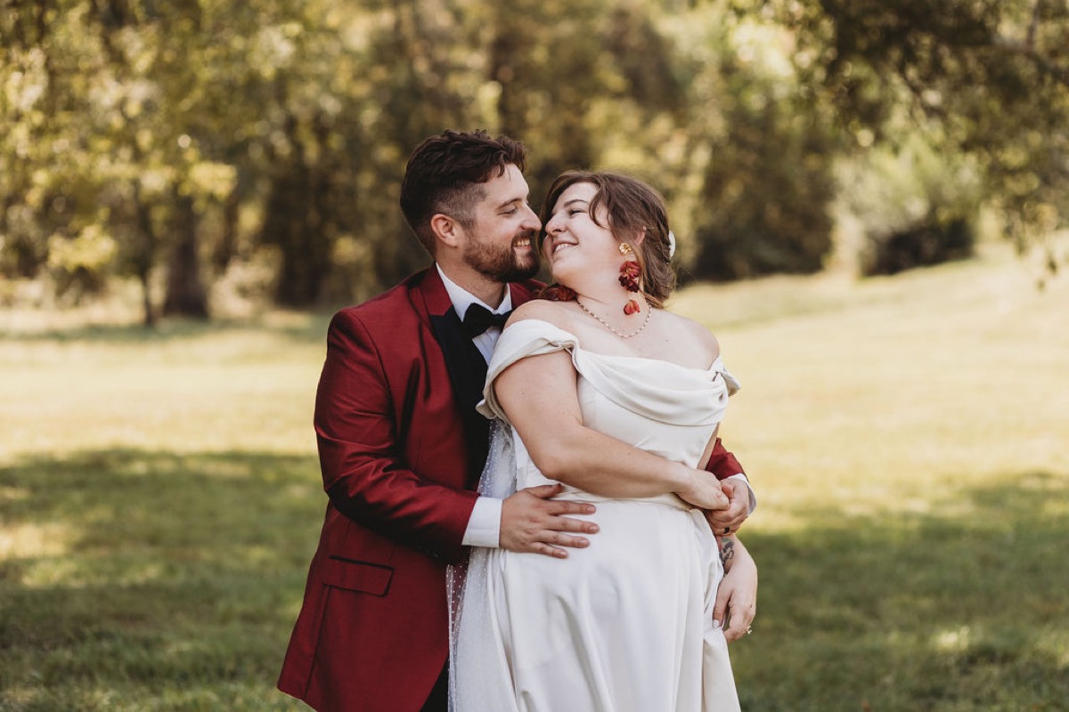 Lauren & Alex smile in a close embrace, her in white and him in a burgundy jacket, at Covey Creek