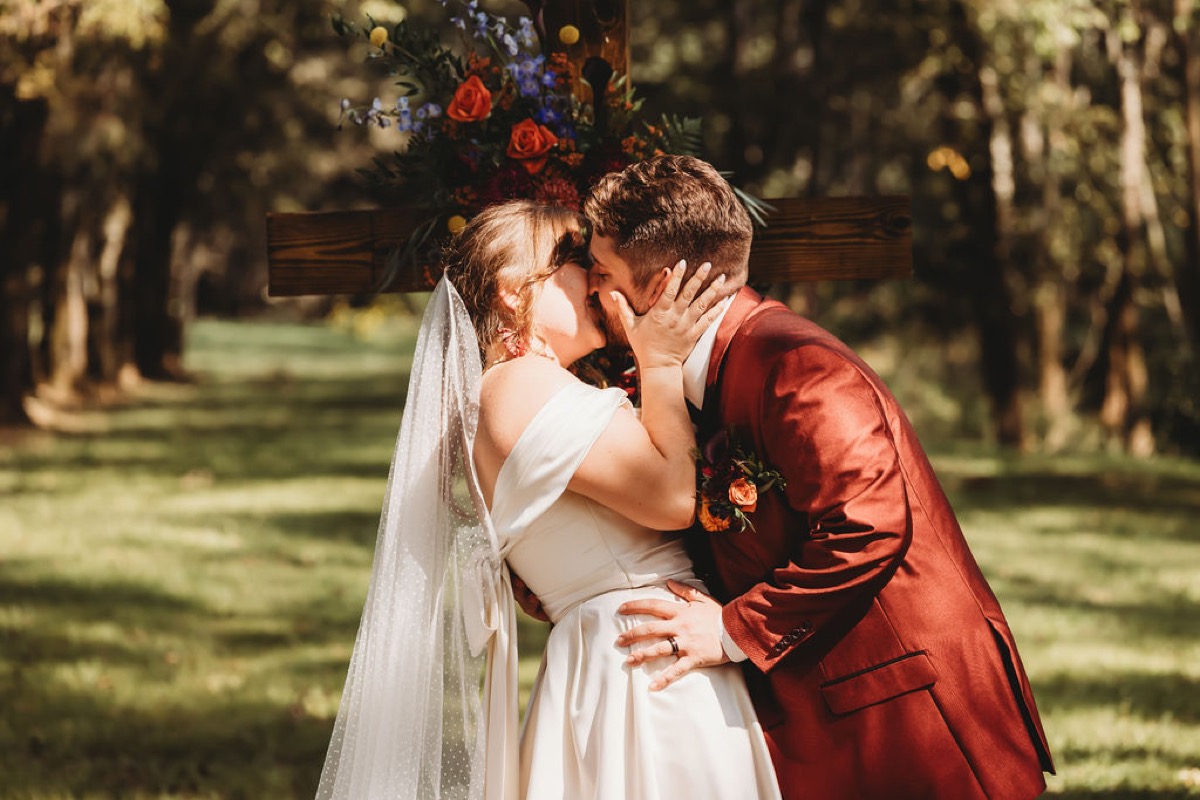 Lauren & Alex share their first kiss before a floral wooden cross at their Covey Creek ceremony
