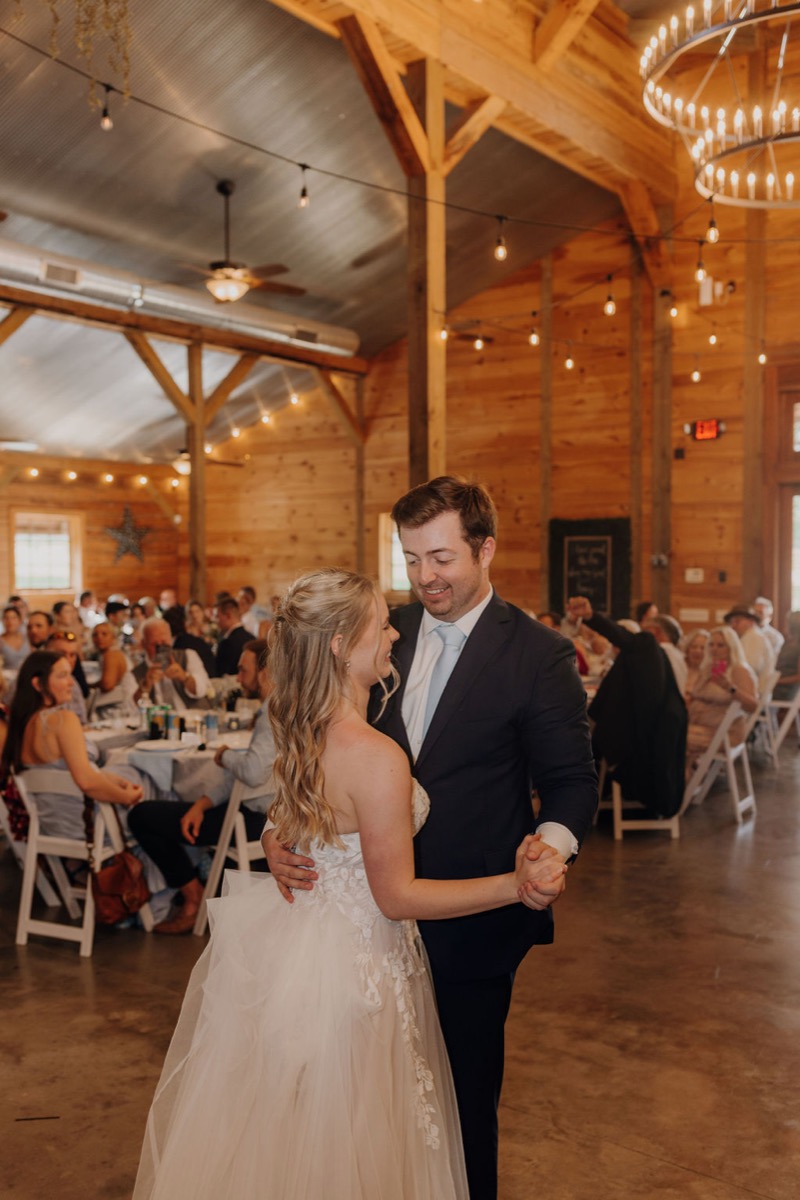 Leah & Gordon share their first dance in Covey Creek’s timber barn beneath a glowing bulb chandelier