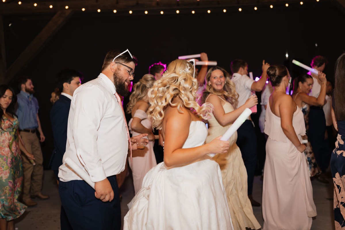 Lilly & Jackson dance with glowing foam sticks under string lights among guests at Covey Creek reception