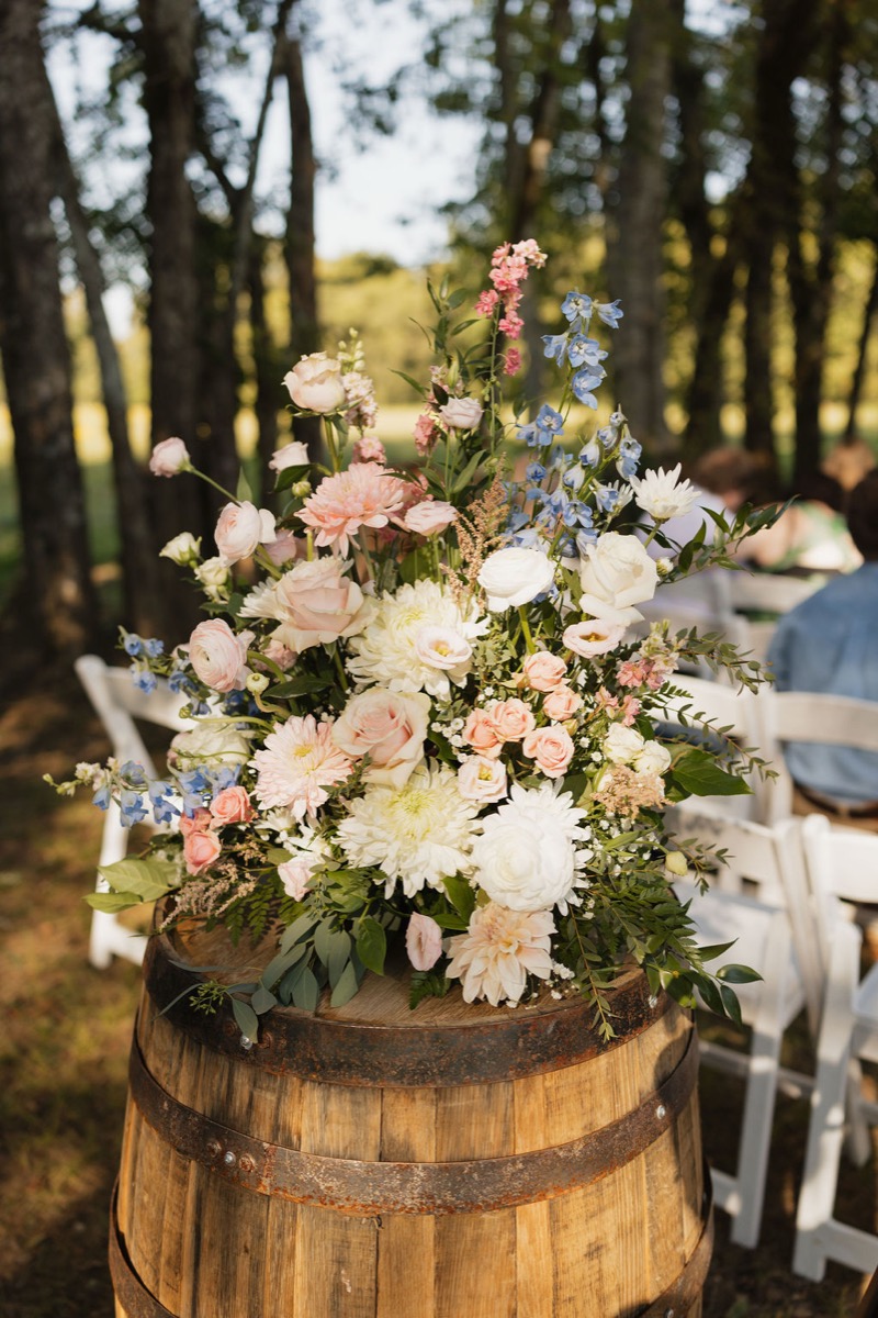 Pink white and blue florals atop a wooden barrel beside white chairs at Lilly & Jackson Covey Creek ceremony